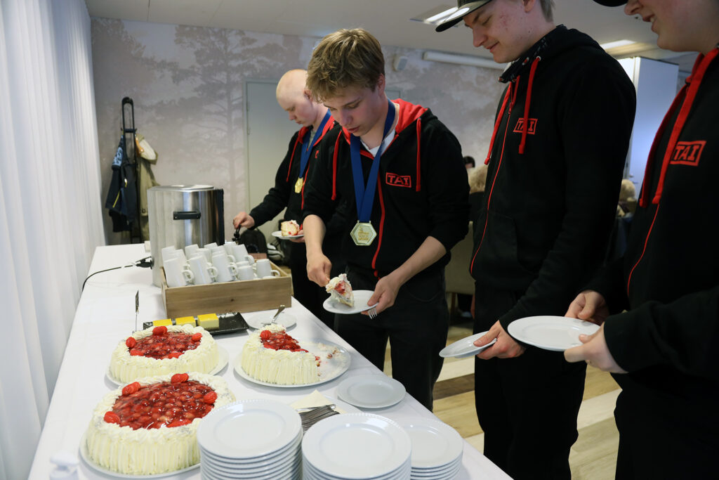TAIn hupppareihin pukeutuneet opiskelijat ottavat kakkua lautaselle.