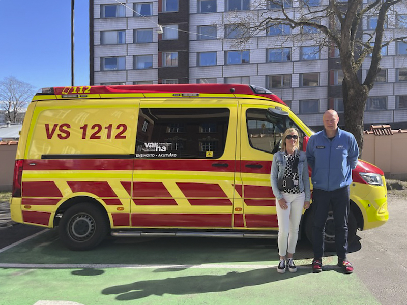 Mies- ja naisoletetut hymyilevät kameralle ambulanssin edessä.