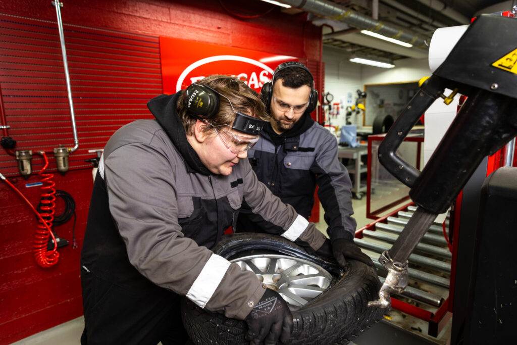 Ajoneuvoalan opettaja ja opiskelija laittavat autonrengasta vanteeseen.